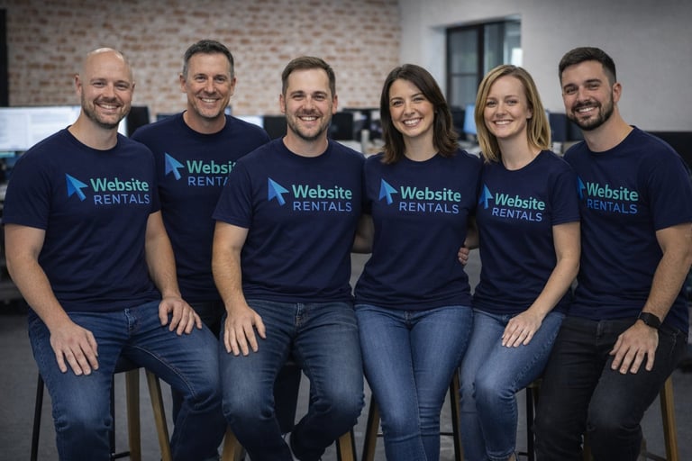 Six team members wearing matching navy Website Rentals t-shirts pose together for a group photo in an office setting.
